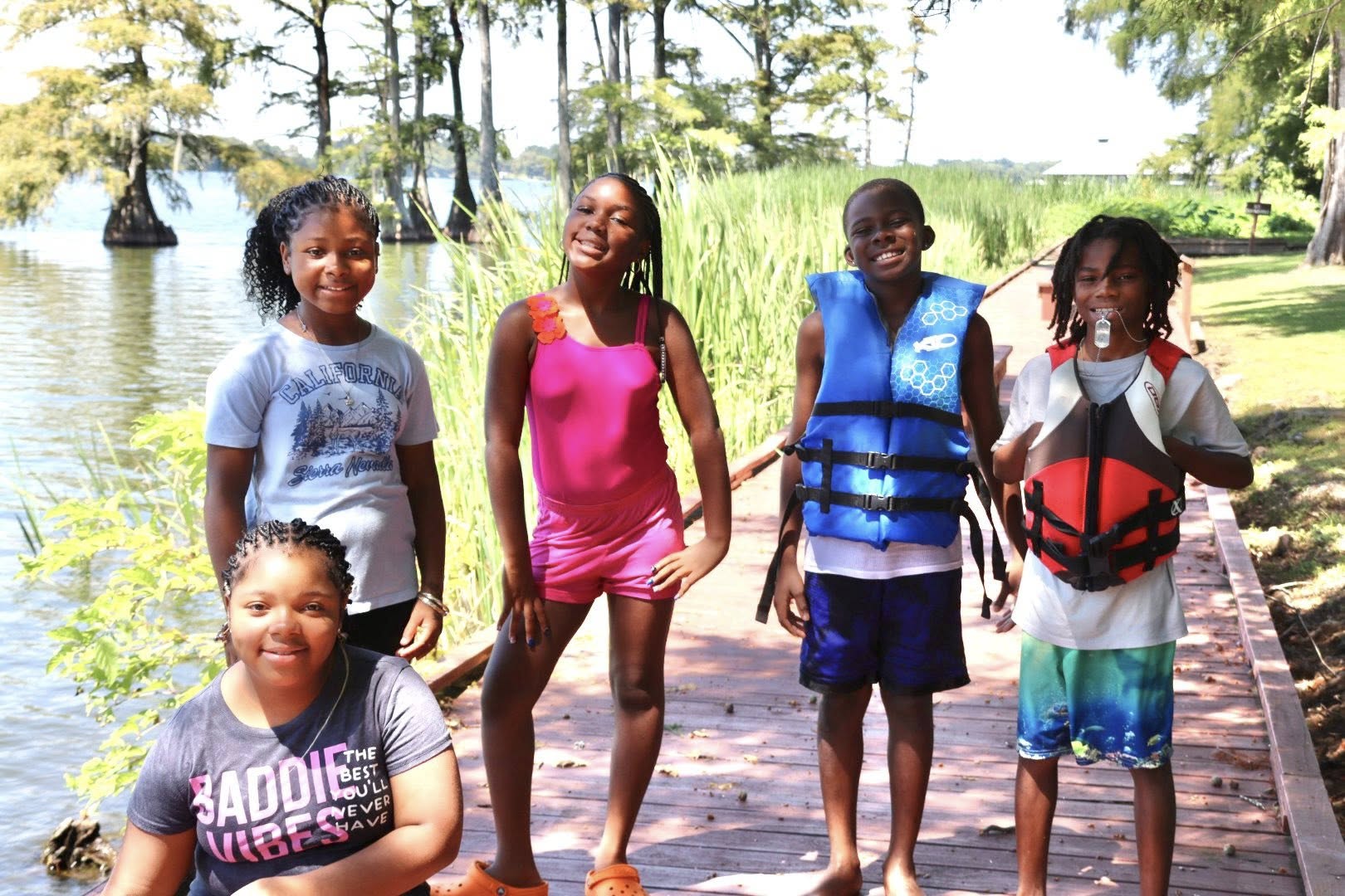 Three girls and two boys posing for a photo beside a lake.